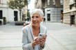 © Davor - Senior businesswoman sitting on bench using smartphone in city