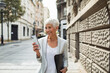© Davor - Senior businesswoman walking in city using smartphone