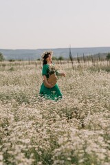 Happy woman in a field of daisies with a wreath of wildflowers on her head. woman in a green dress in a field of white flowers. Charming woman with a bouquet of daisies, tender summer photo