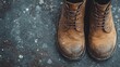 © Dulemegapixel - A pair of well-worn brown work boots positioned neatly on a textured stone floor, showcasing sturdy construction and durability suitable for labor-intensive tasks.