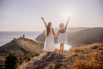 Wall Mural - Two women are standing on a hill overlooking the ocean. They are holding hands and looking out at the water. The scene is peaceful and serene, with the sun shining brightly in the background.