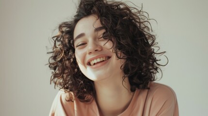 A candid moment capturing a young woman with curly hair, beaming with a wide smile in a sunlit room.