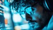 © Dulemegapixel - A blurred close-up shot of an individual in front of a computer monitor, enveloped in blue light, likely performing tasks requiring high concentration.