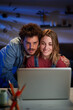 © CarlosBarquero - Vertical two happy young Caucasian people together looking at computer sitting at desk at night room. Smiling millennial affectionate couple at home using laptop. Domestic relations and leisure time