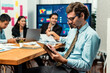 © InfiniteFlow - Portrait of businessman or analyst looking at camera with his colleague analyzing data analysis in dynamic business strategy investment planning meeting. Meticulous