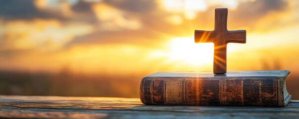 Wooden cross on bible with sunrise background, spiritual concept