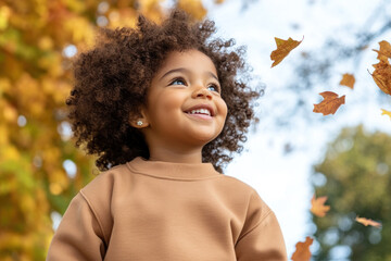 Wall Mural - Afro little girl smiling wearing sweatshirt playing at sunny autumn park