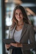 © yj - young professional business woman standing in office. female company executive, smiling businesswoman entrepreneur corporate leader manager looking at camera using tablet.