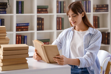 Wall Mural - Happy female student reading books and studying at library