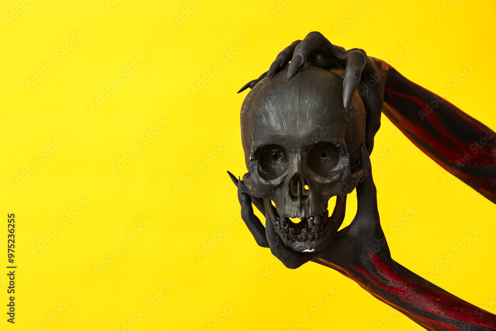 Black witch hands with claws and human skull on yellow background. Halloween celebration