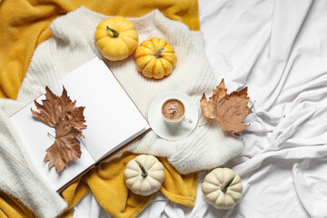 Poster - Cup of tasty pumpkin coffee with autumn leaves, book and warm sweaters on bed at home, top view