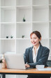 © Satori Studio - A young professional woman in a blazer working on a laptop in a modern office with white shelves in the background.
