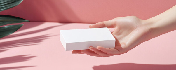 Wall Mural - Hand holding white box on pink background with leaves, minimal design concept