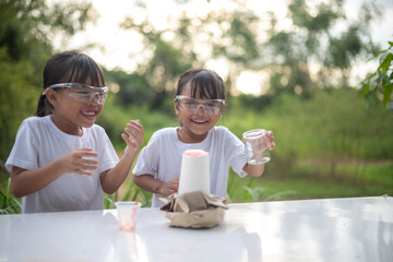 Two young girls excitedly play with a small volcano experiment, laughing as foam erupts.