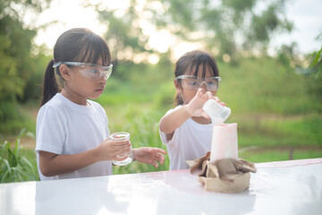 Two young girls excitedly play with a small volcano experiment, laughing as foam erupts.