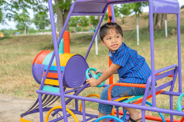 Portrait of a cute little Asian boy. Sitting on play equipment at school or kindergarten or playground. Summer activities, outdoor play, happy, relaxing, and educational ideas.