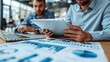 © Suradet Rakha - Businessmen working together with a tablet and laptop, analyzing financial data and strategizing for business growth in an office room. The business team is using digital technology to discuss their m