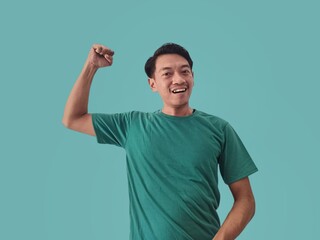 Big win. Excited Asian young man in Tosca shirt celebrating success with raised hands isolated on Tosca background, concept of celebrating victory