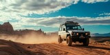 A white jeep is driving through a desert with a cloudy sky in the background. The jeep is covered in dust and he is in the middle of a desert road