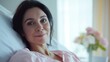 © gn8 - Content Hispanic Woman Relaxing Comfortably in a Bright Room, Featuring Fresh Flowers in the Background, Ideal for Wellness and Recovery Themes