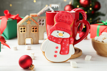 Poster - Delicious cookie in shape of snowman, cup with cocoa and Christmas decor on white wooden table, closeup