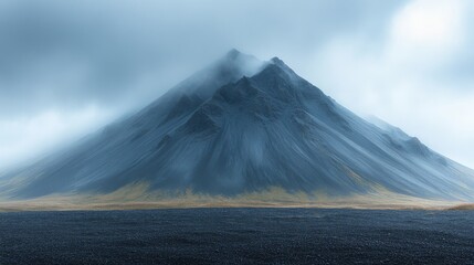 Wall Mural - Majestic, mist-covered mountain with steep slopes rises against a cloudy sky, surrounded by barren, rocky terrain and patches of grass