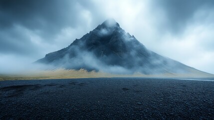 Wall Mural - Towering, mist-shrouded mountain rises over a rocky ground, with dark clouds enveloping its peak, creating a mystical atmosphere