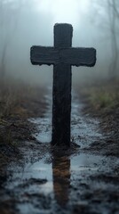 Wall Mural - Weathered wooden cross stands prominently on a muddy path amidst a foggy, overgrown landscape, evoking solemnity and mystery