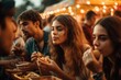 © Nad - people sitting at a table eating food together at a festival or gathering, with lights in the background,
