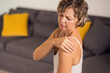 © Aleksej - Woman feeling shoulder pain, sitting on sofa. Female Massaging Painful Area And Frowning, Suffering Osteoporosis Or Arthritis. People and healthcare concept