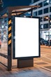 © BISO - A mockup of a blank white vertical digital billboard poster at a city street bus stop sign at night. The billboard is illuminated.