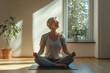 © Alexandra - Senior woman is practicing yoga at home, sitting in a lotus position on a mat and doing a breathing exercise