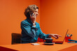 © Jacob Lund - Business owner talking on smartphone while pointing at laptop in a bright orange office