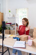 © Pichsakul - A young woman wearing a red sweater is filming content for her online clothing business. She is speaking in front of a camera, surrounded by boxes