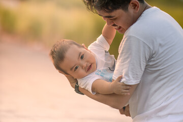 father cradling baby boy and baby boy smiling at camera. father and baby boy wearing white t-shirts. photo with natural background with sunlight in the afternoon.