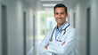 © Julia - Portrait of friendly male doctor in workwear with stethoscope on neck posing with folded arms in clinic interior, looking and smiling at camera, copy space