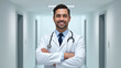 © Julia - Portrait of friendly male doctor in workwear with stethoscope on neck posing with folded arms in clinic interior, looking and smiling at camera, copy space