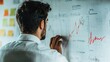 © Natpasit - A man in a plaid shirt stands in front of a wall covered with data charts and graphs, deeply focused in a modern office space.