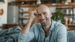 © Samady - Happy bald man breast cancer patient survivor sitting on couch at home. Smiling positive hairless lady touching shaved head feeling optimistic about recovery and remission relaxing at home. Vertical