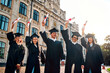 © HBS - Happy graduate students standing in black robes and raising their diplomas up at graduation ceremon. Bright future and education.