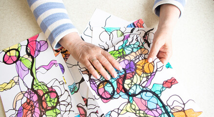 Close-up of female hands drawing neurographic art. Mental health, adult fine motor skills, creativity, psychology. Abstract neurographic drawing with a marker, colored pencils. Art therapy. psychology