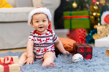 Baby in red hat on Christmas Day, filled with camera, presents and Christmas tree.