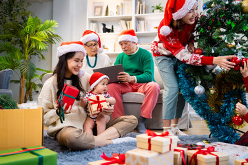 Asian family on Christmas Day. Everyone is happy together in a Christmas themed room filled with presents and orange lights.