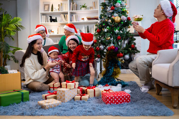 Asian family on Christmas Day. Everyone is happy together in a Christmas themed room filled with presents and orange lights.