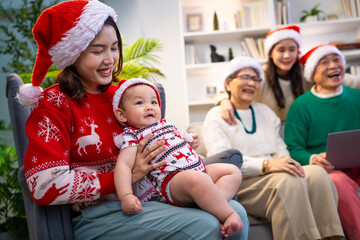 Asian family on Christmas Day. Everyone is happy together in a Christmas themed room filled with presents and orange lights.