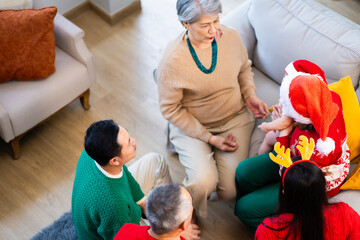 Asian family on Christmas Day. Everyone is happy together in a Christmas themed room filled with presents and orange lights.