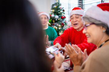 Asian family on Christmas Day. Everyone is happy together in a Christmas themed room filled with presents and orange lights.