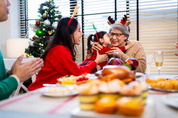 Asian family on Christmas Day. Everyone is happy together in a Christmas themed room filled with presents and orange lights.