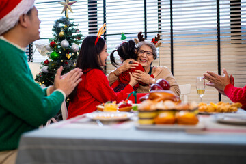 Asian family on Christmas Day. Everyone is happy together in a Christmas themed room filled with presents and orange lights.