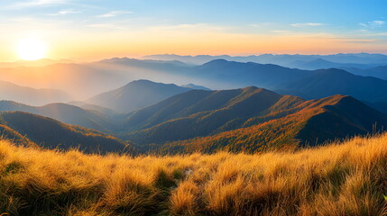 Landscape of majestic mountain ranges at sunrise, with golden sunlight casting soft rays over distant hills and valleys. The foreground consists of a grassy ridge covered in golden autumn hues.